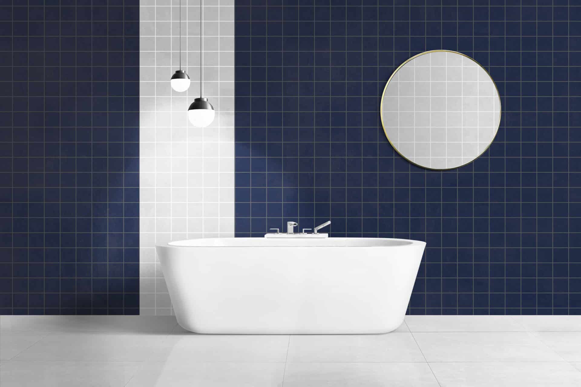 Modern bathroom with a freestanding white bathtub, navy and white tiled wall, round mirror, and pendant lights in a minimalist interior design.